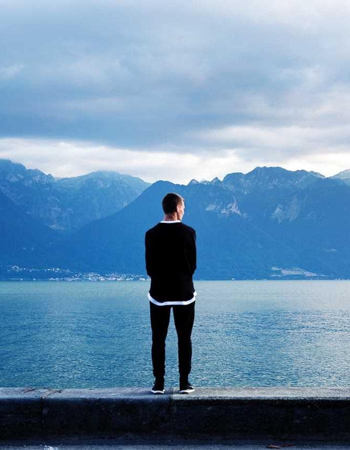 Man standing at the edge of a lake facing the mountains